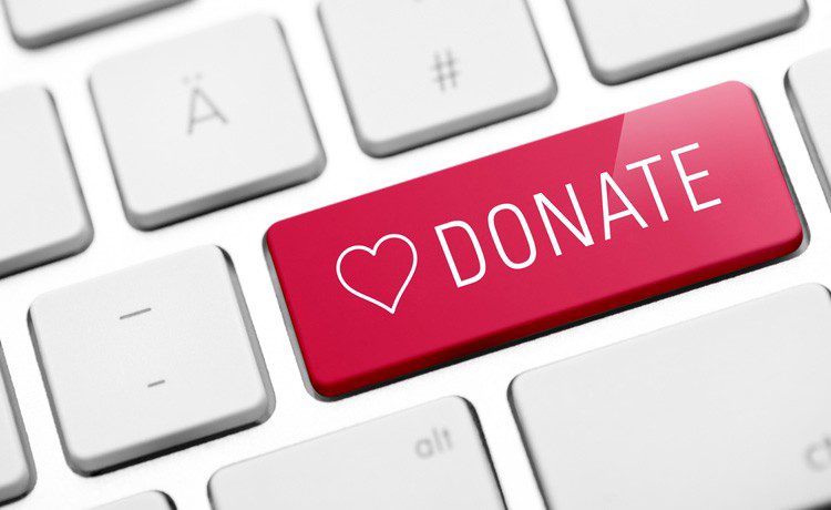 A computer keyboard features a large red key with a heart icon and the word "DONATE." The mood conveys urgency and encouragement to contribute.