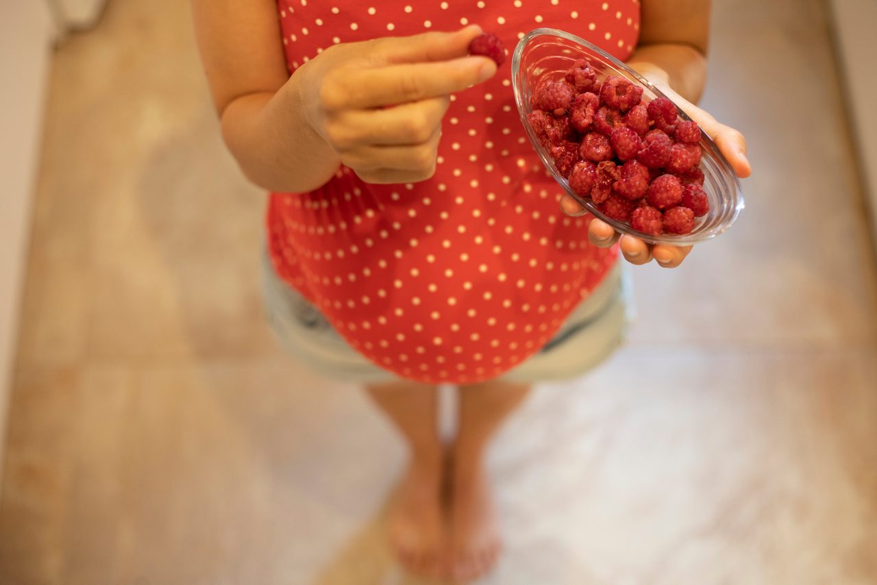 Unrecognizable pregnant young woman holding a bowl with fresh, ripe raspberries.