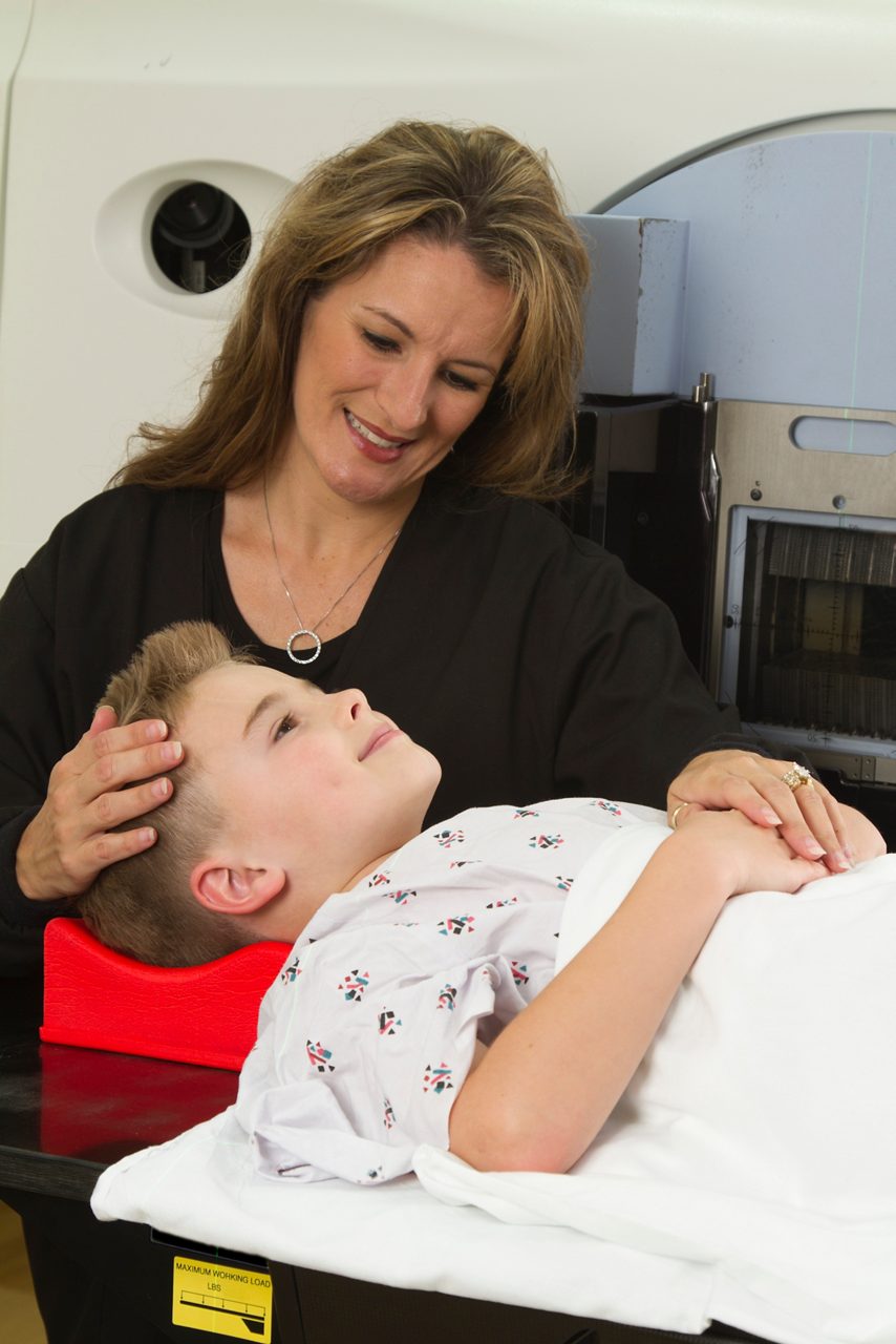 Medical Dosimetrist / Radiation Therapist preparing a young pediatric patient for cancer treatment on a lineal accelerator showing compassion.