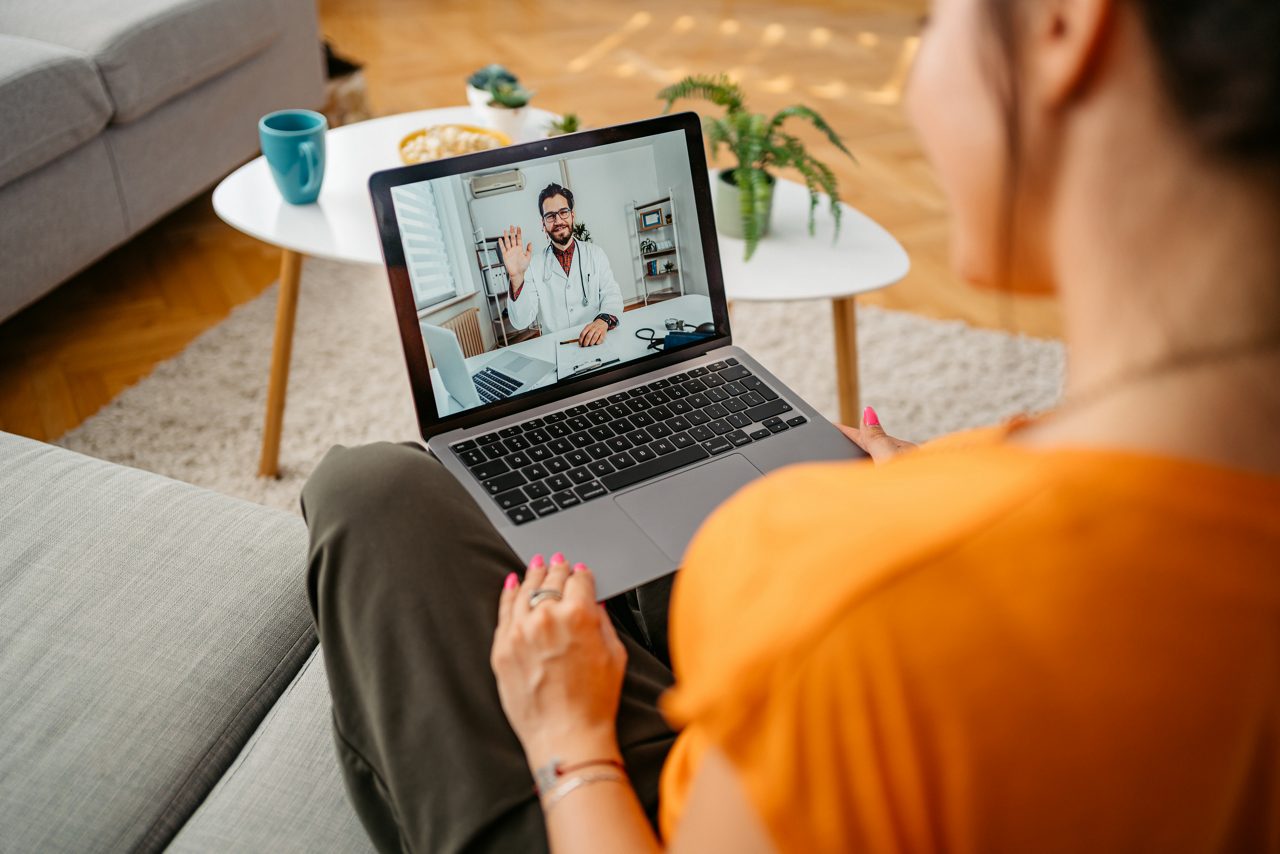 Beautiful young woman having a doctor's appointment online over the laptop, while sitting at home.