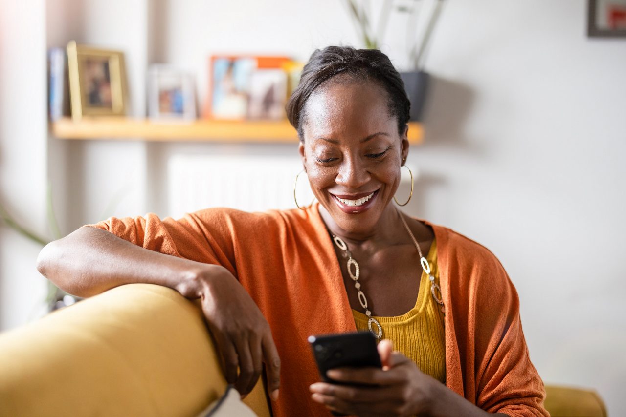 Mature woman using mobile phone while relaxing on a sofa at home