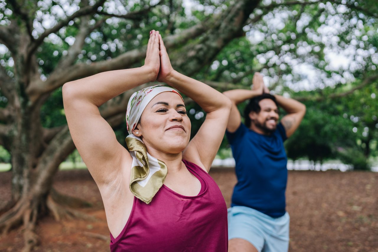 A mature woman who is battling cancer doing yoga with her husband at park