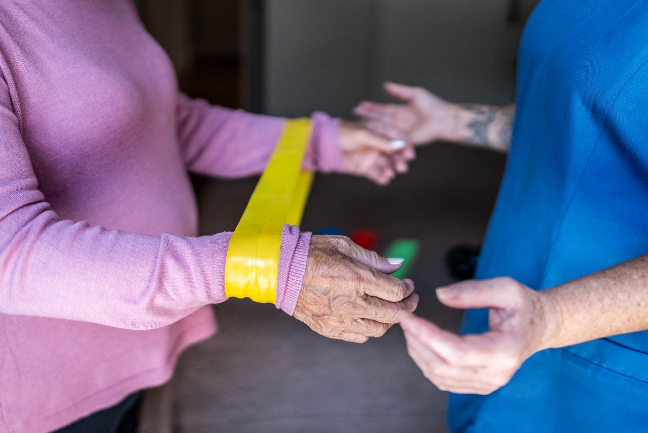 Senior woman doing exercises with rubber band during house call