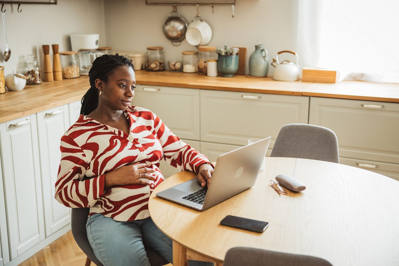Young pregnant woman working on laptop at kitchen counter.