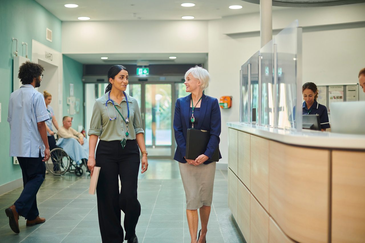Two people walking through hospital administration hallway