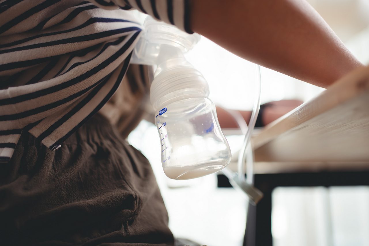 Close up shot of woman pumping breast milk using electric double breast pump at home office. 