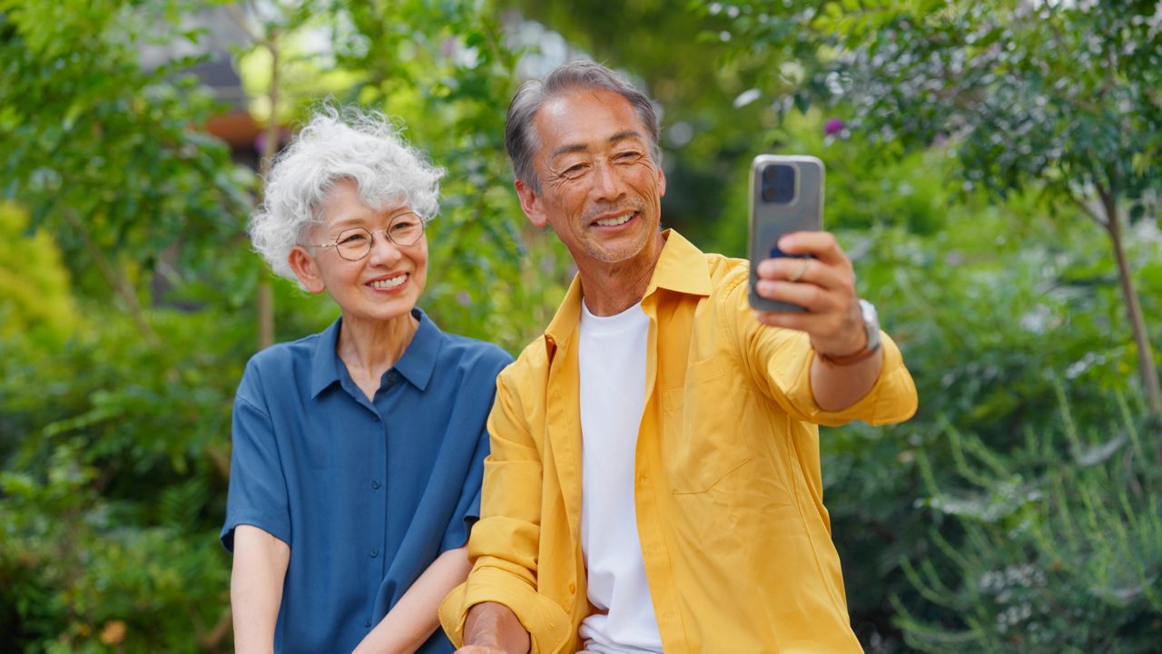Senior couple sitting at bench and taking selfies with mobile.