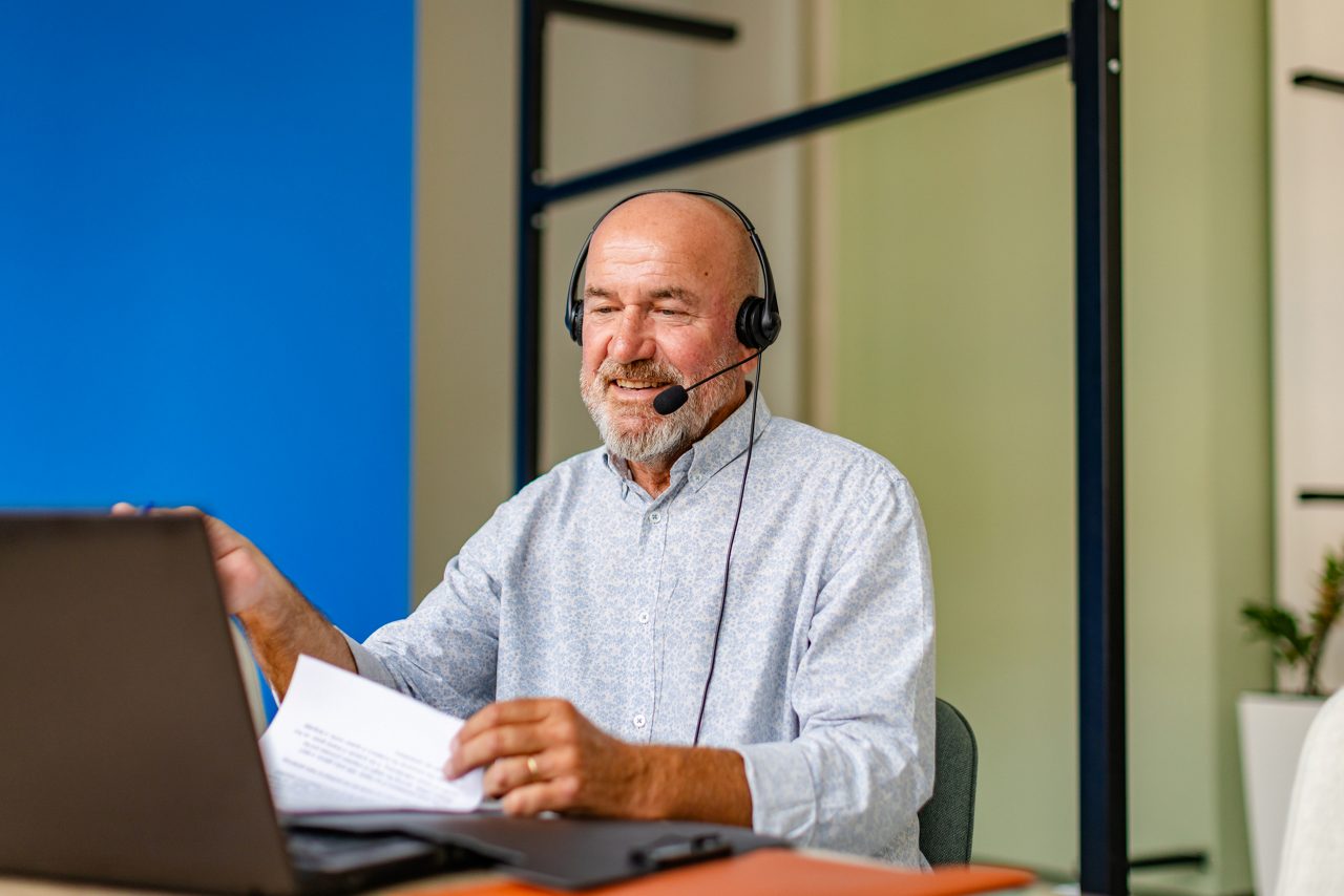 Elderly man smiling during online call while sitting at office desk