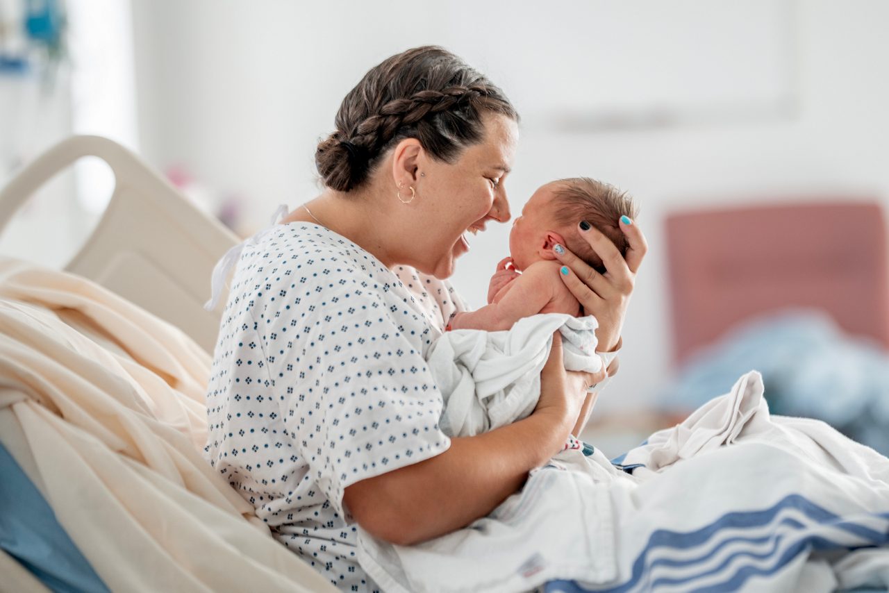 A loving mother cradles her newborn baby in a hospital bed, sharing a joyful, intimate moment of bonding and new parenthood.