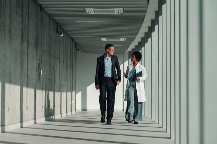 Diverse colleagues walking through modern hallway, discussing business, healthcare, or research collaboration. Two professionals brainstorming ideas