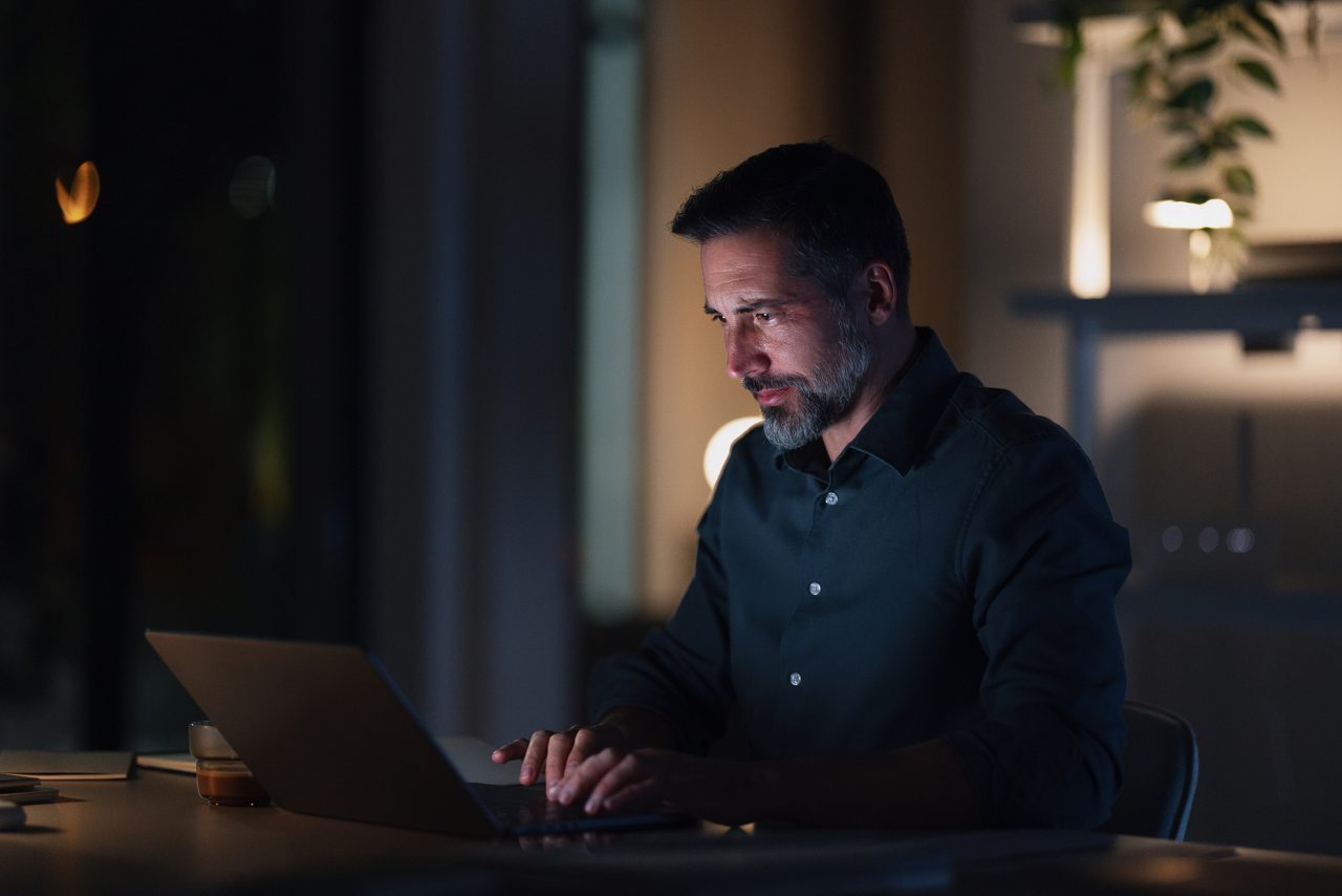 A focused businessman works late at night in a quiet, modern office. The laptop glow lights his face as he concentrates on tasks, reflecting dedication, late hours, and professional effort.