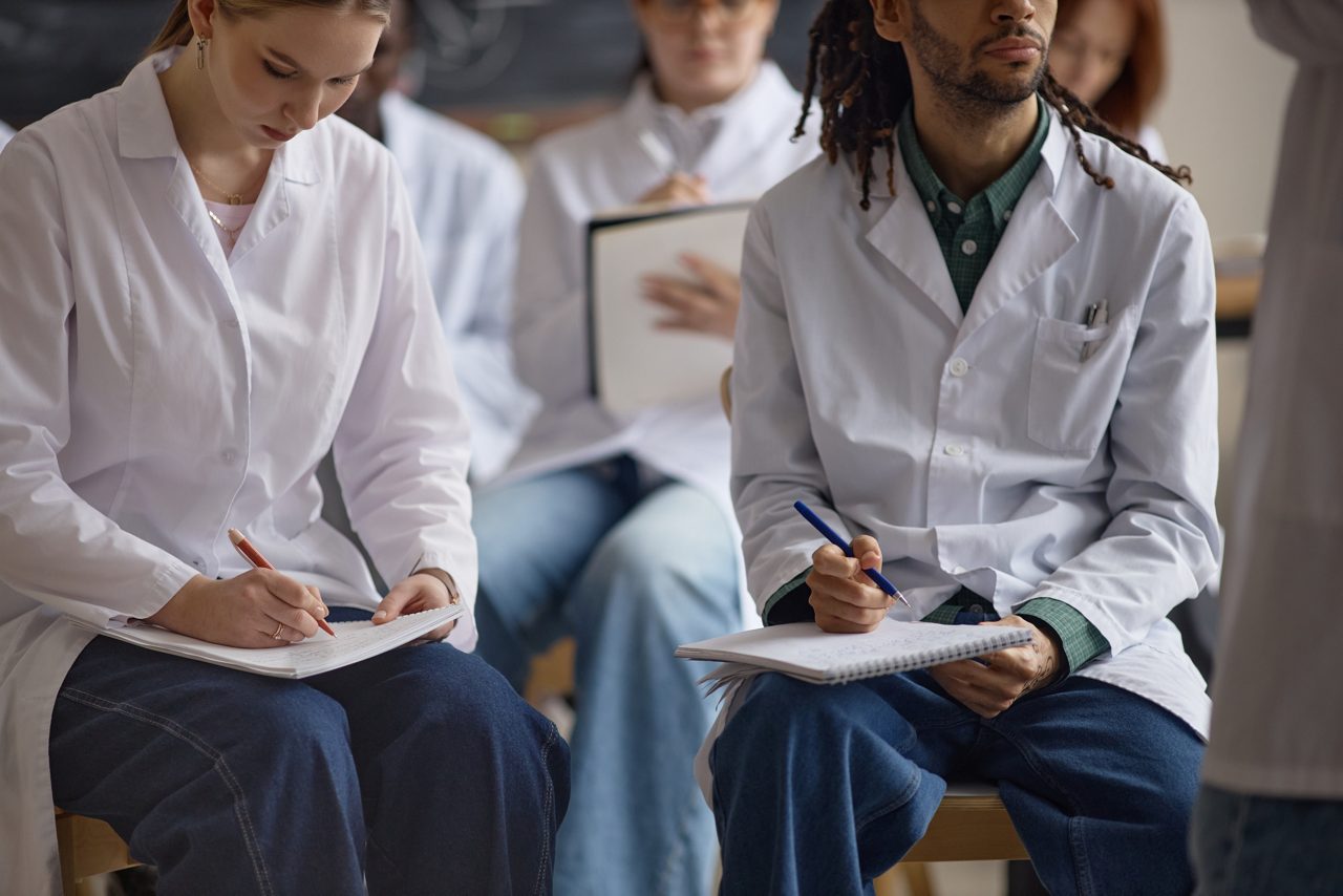 Diverse young adult medical students taking notes during clinical training session, studying patient care concepts. Useful for healthcare education, medical school marketing, teamwork content