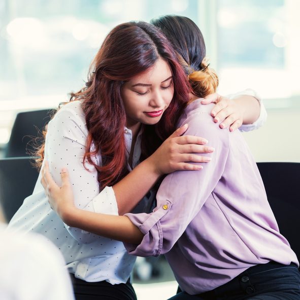 A woman hugs her friend during a group therapy or support group meeting.