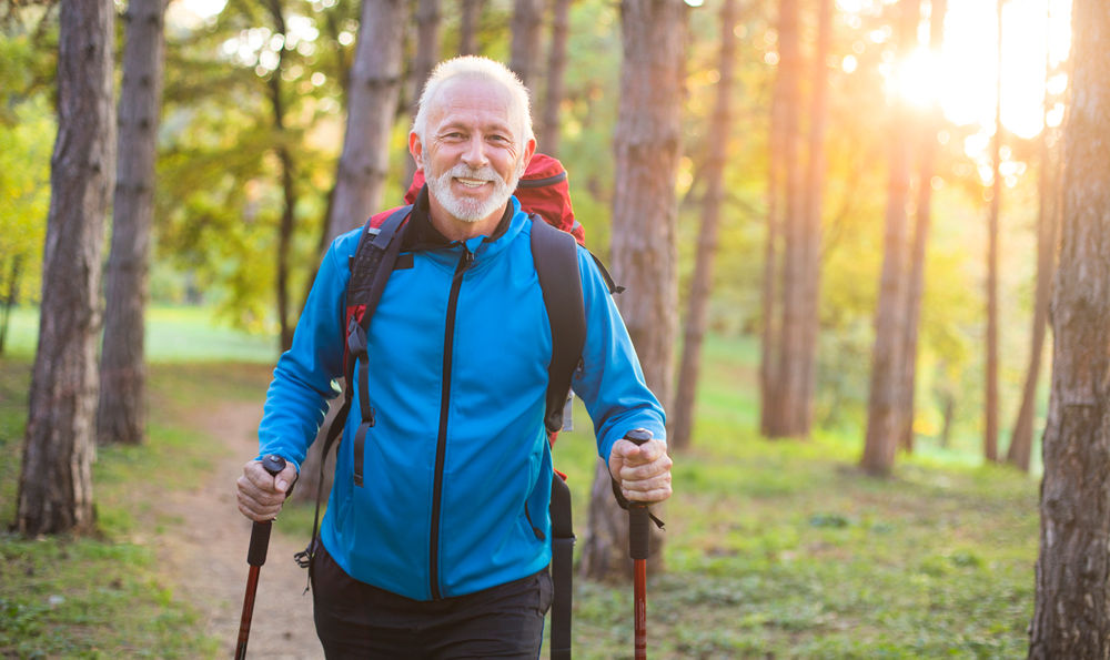 Senior man with arthritis takes a long hike in the forest.
