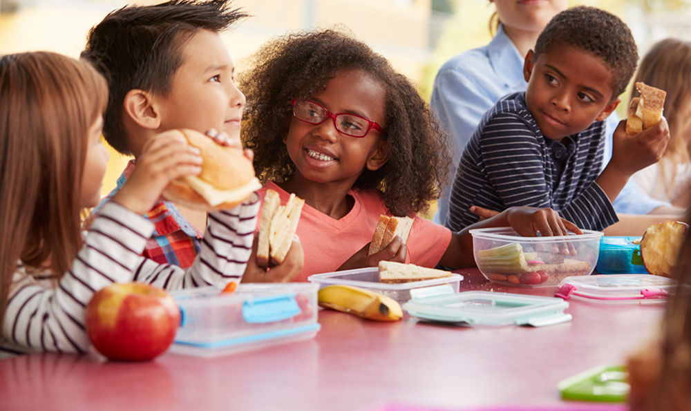 A group of elementary age children enjoy lunch in the cafeteria.
