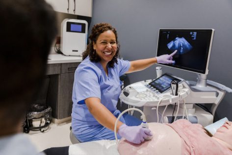Health care worker smiling and pointing at ultrasound screen