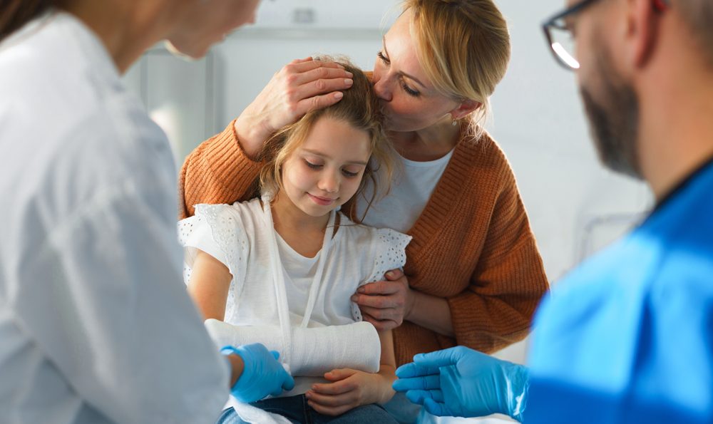 Mother kissing daughters head while she is in a cast in the emergency room.