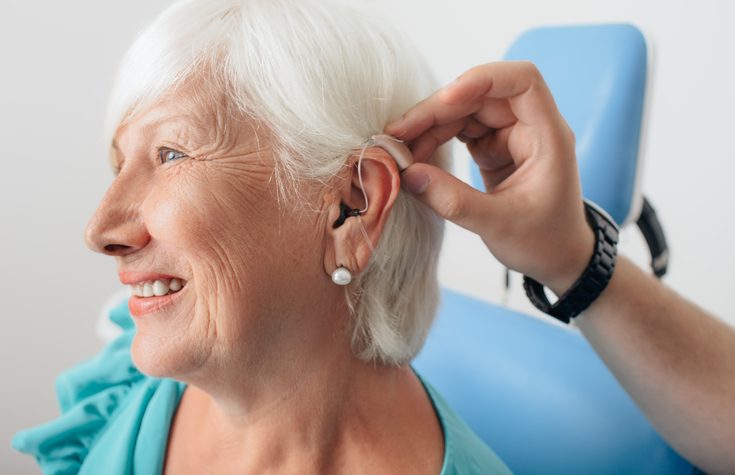 A mature woman is fitted for a hearing aid.