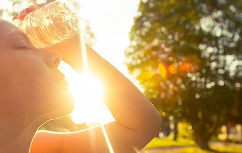 Woman using water bottle to cool down. Fitness and wellbeing concept with female athlete cooling down on a city street. She is holding a water bottle to her head to cool down. The sun is low creating long shadows and some lens flare. Copy space