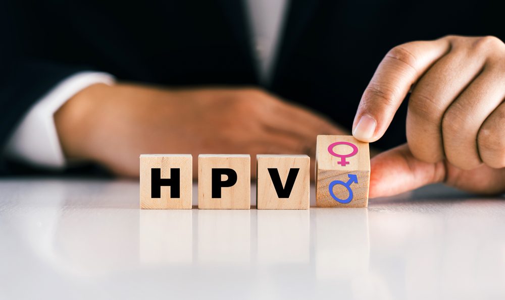 A man spells out HPV in small wooden blocks on a table.