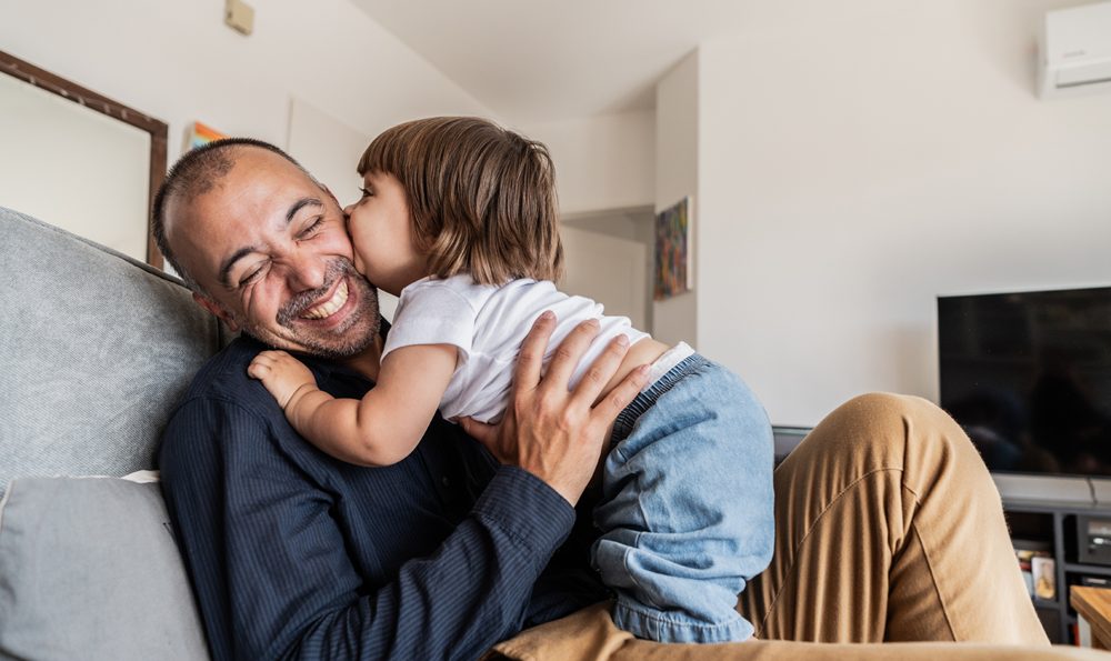 Man smiles as he receives a kiss from his toddler.