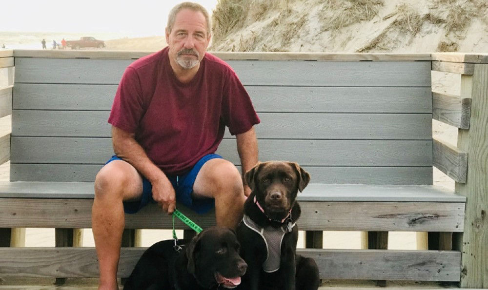 Keith sitting on a bench holding his dogs.