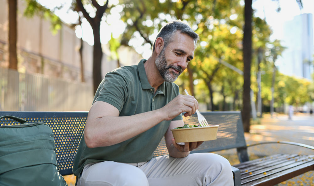 Man eating a salad outside on a bench.
