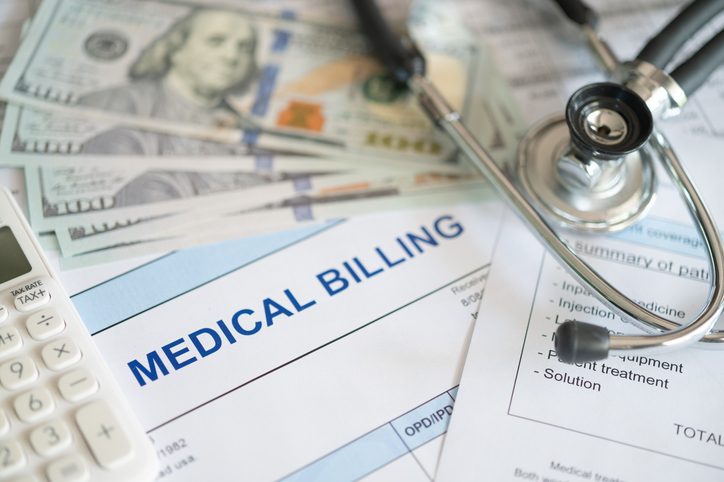 Medical bills, a calculator, money and a stethoscope are shown