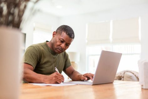Veteran sitting at a desk writing in front of a laptop.