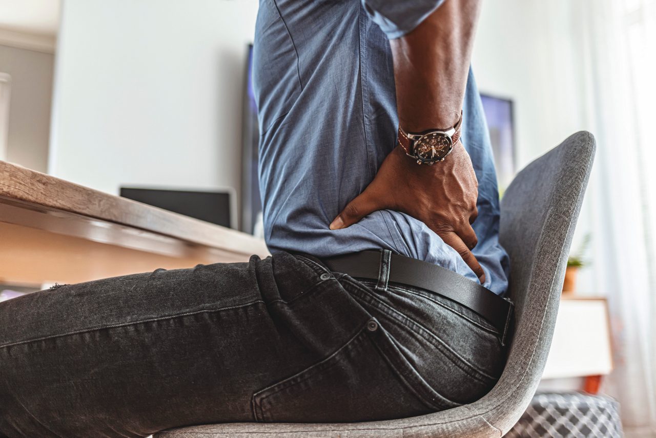 Businessman working sitting at desk feels unhealthy suffers from lower back pain. Damage of intervertebral discs, spinal joints, compression of nerve roots caused by wrong posture and sedentary work.