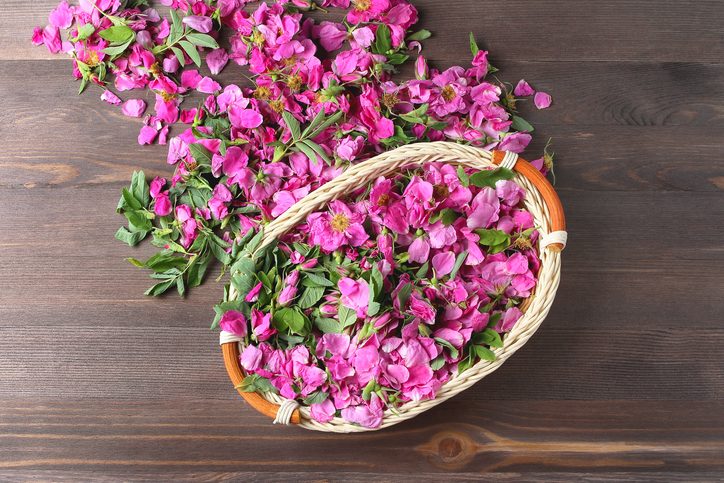 wicker basket with rose petals and flowers in pink on a wooden background. simple flat lay composition.