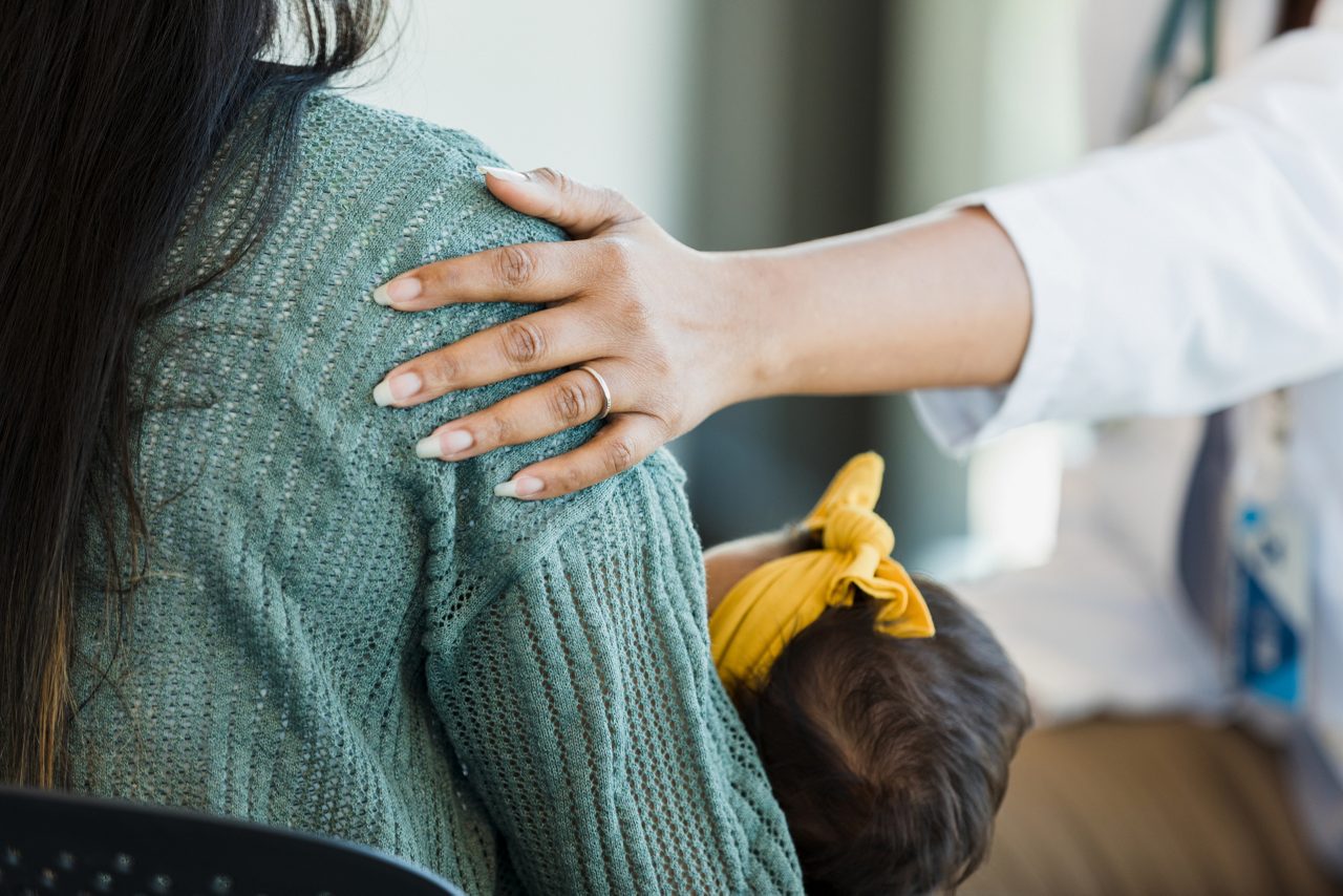 Unrecognizable person places hand on a mother's shoulder as she offers comfort and support.