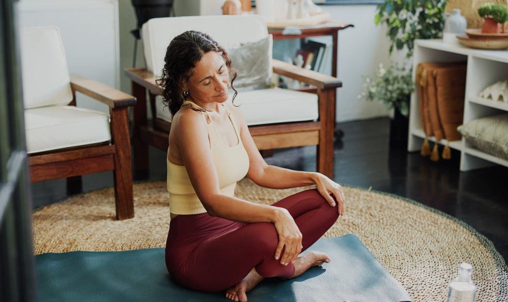 Woman sitting on a yoga mat and stretching her neck.