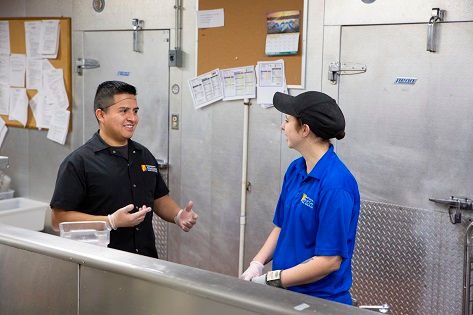 Two food service workers talking to each other.