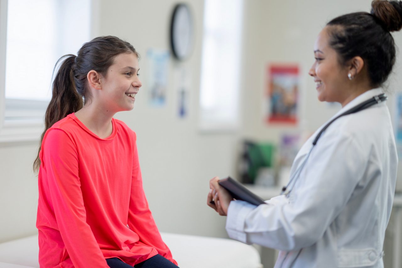 A smiling teenage girl interacts with a caring female doctor in a bright, welcoming medical office, conveying trust and professional care.