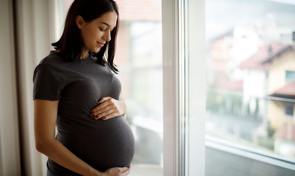 A pregnant woman looking down and holding her stomach.