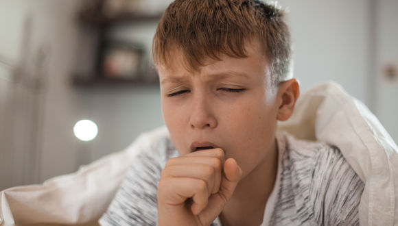 Boy with walking pneumonia coughs in bed.